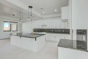 Kitchen featuring tasteful backsplash, a center island with sink, hanging light fixtures, sink, and white cabinets