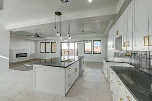 Kitchen featuring white cabinetry, a center island with sink, pendant lighting, sink, and light tile floors