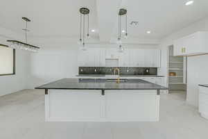 Kitchen with white cabinets, sink, light tile flooring, and a kitchen island with sink