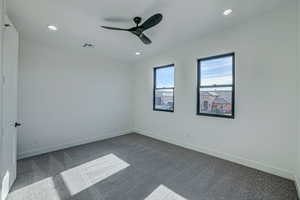 Empty room featuring ceiling fan and dark colored carpet