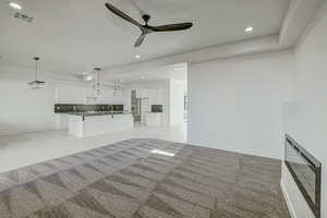 Unfurnished living room with ceiling fan, light carpet, and sink