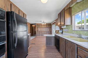 Kitchen featuring pendant lighting, black appliances, wood-type flooring, a notable chandelier, and sink