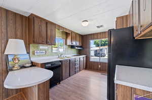 Kitchen featuring backsplash, black appliances, light wood-type flooring, sink, and wooden walls