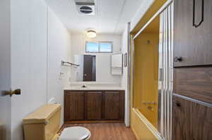 Full bathroom featuring shower / bath combination with glass door, toilet, hardwood / wood-style floors, vanity, and a textured ceiling