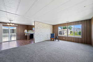 Unfurnished room featuring a notable chandelier, wooden walls, and dark colored carpet