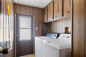 Clothes washing area featuring cabinets, separate washer and dryer, hookup for a washing machine, and wood walls