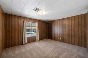 Unfurnished room featuring wooden walls and carpet flooring