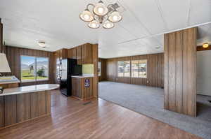 Kitchen with a notable chandelier, black refrigerator, hardwood / wood-style floors, and wood walls