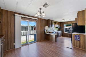 Kitchen featuring a textured ceiling, dark hardwood / wood-style floors, decorative light fixtures, wood walls, and a chandelier