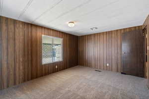 Empty room with wooden walls, a textured ceiling, and carpet floors