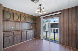 Spare room with dark wood-type flooring, wood walls, and an inviting chandelier