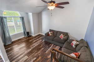 Living room with dark wood-type flooring, ceiling fan, and vaulted ceiling