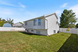 Rear view of house with central air condition unit and a lawn