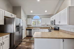 Kitchen featuring kitchen peninsula, dark wood-type flooring, appliances with stainless steel finishes, sink, and lofted ceiling