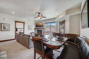 Dining room featuring ceiling fan, a fireplace, and light colored carpet