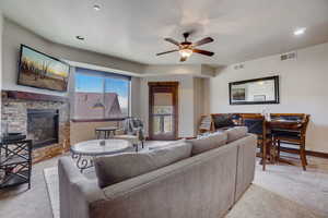 Living room featuring light carpet, a fireplace, and ceiling fan