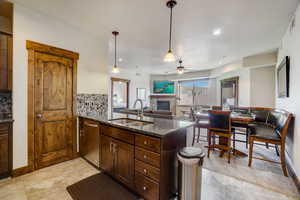 Kitchen featuring light tile flooring, tasteful backsplash, a stone fireplace, stainless steel dishwasher, and sink