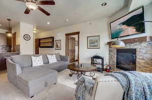 Living room featuring carpet, ceiling fan, and a stone fireplace