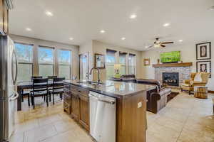 Kitchen featuring a fireplace, stainless steel appliances, a kitchen island with sink, ceiling fan, and light tile floors