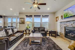 Living room with a stone fireplace, ceiling fan, and light tile flooring