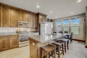 Kitchen featuring light stone countertops, stainless steel appliances, a kitchen island with sink, and light tile floors