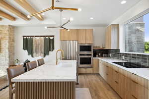 Kitchen featuring a spacious island, sink, appliances with stainless steel finishes, tasteful backsplash, and a breakfast bar area