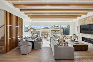 Living room featuring beam ceiling, a stone fireplace, and wood-type flooring