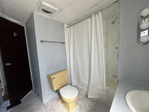 Full bathroom with a textured ceiling, tile floors, shower / tub combo with curtain, sink, and toilet