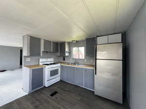 Kitchen featuring stainless steel refrigerator, white gas stove, dark hardwood / wood-style floors, gray cabinets, and sink