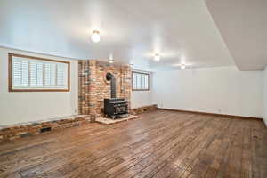 Unfurnished room with brick wall, a wood stove, and wood flooring