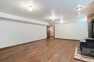 Unfurnished living room featuring brick wall, a wood stove, and hardwood floors