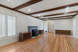 Unfurnished family room with beamed ceiling, light hardwood / wood-style floors, and a wood stove