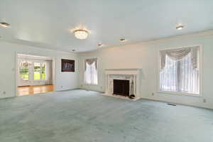 Unfurnished living room featuring a premium fireplace, ornamental molding, carpet, and a notable chandelier