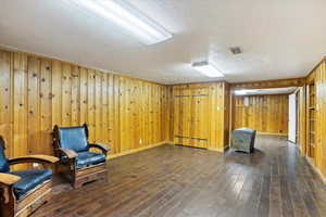 Living area with a textured ceiling, dark wood flooring, and wood walls