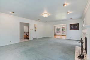 Unfurnished living room featuring carpet flooring, ornamental molding, and a premium fireplace