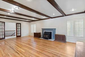 Unfurnished living room with beam ceiling, light hardwood / wood-style flooring, a fireplace, and crown molding