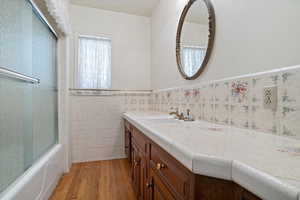 Bathroom featuring enclosed tub / shower combo, hardwood / wood-style floors, oversized vanity, and tile walls