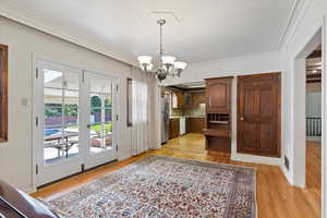 Interior space featuring a notable chandelier, plenty of natural light, ornamental molding, and light wood-type flooring