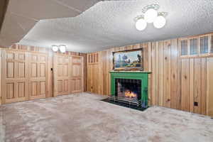 Unfurnished living room featuring carpet flooring, wood walls, a textured ceiling, and a fireplace