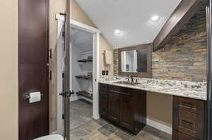 Bathroom featuring tile flooring, vanity with extensive cabinet space, and vaulted ceiling