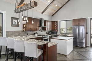 Kitchen with high vaulted ceiling, stainless steel appliances, wood ceiling, and wall chimney exhaust hood