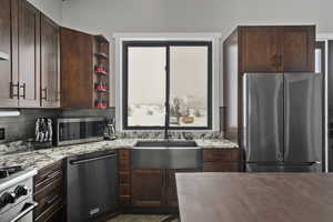 Kitchen featuring dark brown cabinets, stainless steel appliances, light stone counters, backsplash, and sink