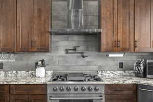 Kitchen with stainless steel range, backsplash, light stone counters, and wall chimney exhaust hood