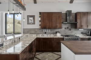 Kitchen with backsplash, range, dark tile flooring, wall chimney exhaust hood, and beam ceiling