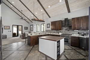 Kitchen with a center island, high vaulted ceiling, wall chimney exhaust hood, dark tile floors, and wooden ceiling