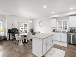 Kitchen with hanging light fixtures, stainless steel dishwasher, white cabinets, wood-type flooring, and sink