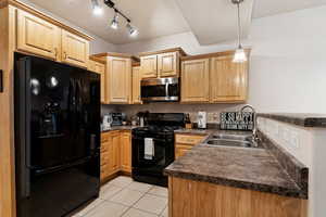 Kitchen featuring decorative light fixtures, black appliances, track lighting, sink, and light tile floors