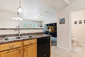 Kitchen with sink, black dishwasher, decorative light fixtures, and light tile floors