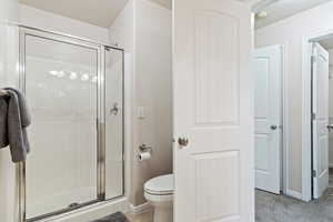 Bathroom featuring a shower with door and toilet