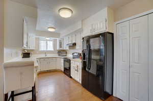 Kitchen featuring a textured ceiling, light hardwood / wood-style flooring, black appliances, white cabinets, and sink